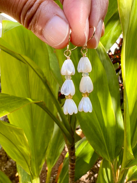Fingertips holding pair of gold-filled french wire earrings. Stack design. 3 MOP carved pikake with one citrine & one moonstone rondels between each bud against Ti leaf plants