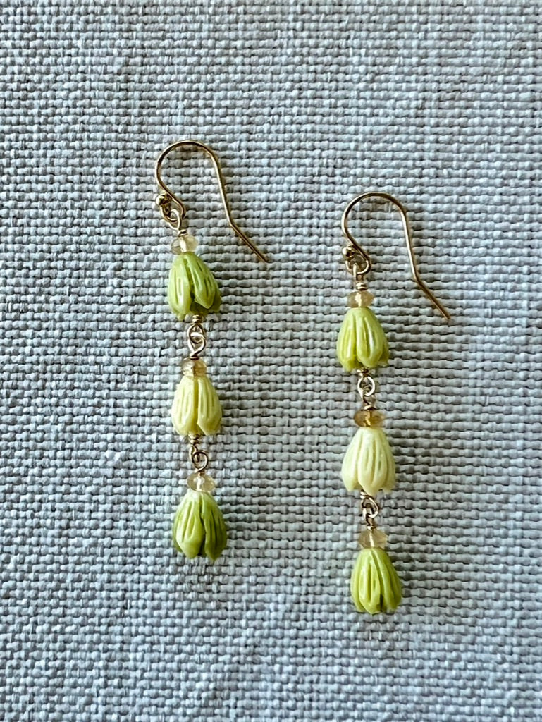 Pair of green pikake bud earrings on textured material background
